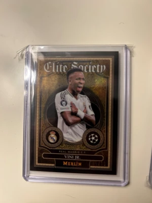 Fotbollskort med Vini Jr. från Real Madrid C.F. ur Topps Merlin Elite Society-serien. - Fotbollskort med Vini Jr. från Real Madrid C.F. ur Topps Merlin Elite Society-serien.  Numrerat 05/10 – endast 10 exemplar.  Kortet lades direkt i sleeve och cardloader efter öppning och har förvarats skyddat sedan dess.  Kortet är i mycket fint skick och kan vara intressant för framtida PSA-gradering.