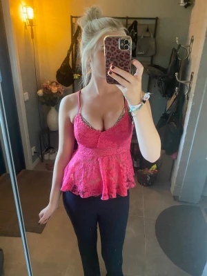 Rosa spetslinnetopp med volang - Säljer en snygg rosa linnetopp med tunna axelband och volang nedtill. Toppen är i spetsmaterial med blommigt mönster och har en feminin, croppad passform. Perfekt för dig som vill sticka ut lite extra med en färgglad och trendig topp.