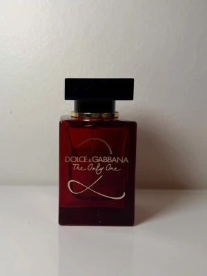 Dolce & Gabbana The Only One parfym - Säljer en lyxig halvfull parfym från Dolce & Gabbana, The Only One. Flaskan är djup röd med gulddetaljer och har en elegant, fyrkantig form med svart lock. Perfekt för dig som vill ha en ikonisk doft i snygg design.