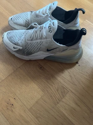 Nike Air Max 270 vita sneakers - Nike Air Max 270 sneakers i vitt med svarta detaljer och synlig Air-enhet i hälen. Ovandelen är i mesh för bra ventilation och har klassisk Nike-logga på sidan och tån. Skorna har snörning och en sportig, modern siluett. Dom behöver nog bara en ordentlig tvätt sen ser dom bättre ut