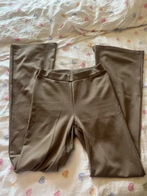 Beiga raka leggings - Säljer ett par beiga leggings med rak passform och bred resår i midjan. Materialet är mjukt och stretchigt, perfekt för en avslappnad look. Inga synliga detaljer eller loggor. Passar till många olika stilar.