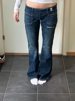 Mörkblå bootcut jeans med slitningar - Säljer ett par mörkblå bootcut jeans med snygga slitningar och kontrastsömmar från Gina. Jeansen har låg midja, två framfickor och dubbla knappar i linningen. Perfekta för en avslappnad och trendig look. Använda max 2 gånger. 