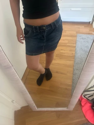 Mörkblå jeanskjol med fickor - Säljer en mörkblå jeanskjol i klassisk modell med framfickor och knappstängning. Kjolen är kort och har en snygg, enkel design som passar till det mesta. Perfekt för dig som gillar en avslappnad men trendig stil.