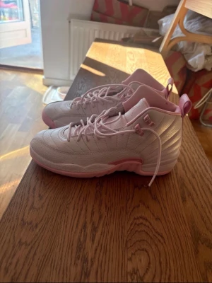 Air Jordan 12 Retro GS ”Pearl pink” Unisex Storlek EUR 40 - Säljer ett par snygga höga sneakers i ljusrosa och vitt med matchande rosa snören och detaljer. Skorna har en vadderad plös och sula i rosa, samt en klassisk siluett med paneler i läder. Perfekta för dig som vill sticka ut med en fräsch och trendig look. De är helt nya från USA min faster köpte till mig men de var fel storlek 