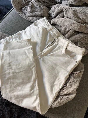 Vita raka jeans från H&M - Säljer ett par vita jeans från H&M i rak modell. Jeansen har klassisk femficksdesign, dragkedjegylf och silverfärgade nitar. Materialet är kraftigt bomullstyg som ger en snygg och stilren look.