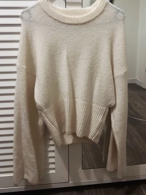 Vit stickad tröja från Gina Tricot - Mysig vit stickad tröja från Gina Tricot i ullblandning. Tröjan har en bred ribbad mudd i midjan och vid ärmsluten, samt en rund halsringning. Perfekt för kalla dagar och enkel att styla till olika outfits.