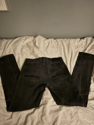 Nuddie jeans  - Säljer ett par svarta slim fit jeans med klassisk femficksdesign och raka ben. Jeansen har bälteshällor och subtila slitningar för en cool look. Perfekta till en avslappnad stil och passar till det mesta i garderoben. Hör av er vid frågor😃