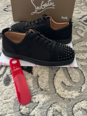 Christian Louboutin helt nya aldrig använd säljs pga av flytt billigt  - Säljer ett par svarta sneakers från Christian Louboutin med mattsvarta nitar på tån och svarta skosnören. Skorna har en låg profil och är tillverkade i mocka och läder för en lyxig känsla. Perfekta för dig som vill sticka ut med en edgy stil.