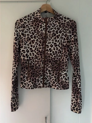 Leopardmönstrad jacka med dragkedja - Säljer en leopardmönstrad jacka med hel dragkedja framtill. Jackan har lång ärm och är figurnära i modellen. Materialet känns mjukt och stretchigt, perfekt för dig som vill sticka ut lite extra. Två fickor framtill med dragkedja.