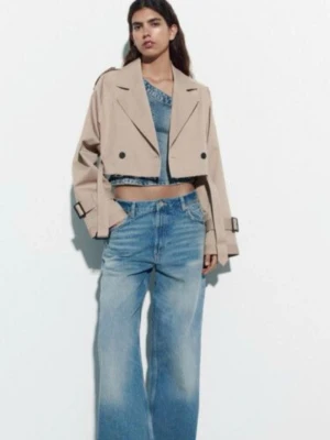 Kort beige trenchcoat med rå kant - Trendig cropped trenchcoat i beige med rå, fransad nederkant och breda slag. Jackan har dubbelknäppning, bälte i midjan och justerbara spännen vid ärmsluten. Perfekt för dig som gillar en edgy och modern stil. Materialet är klassisk trenchcoat-bomull.