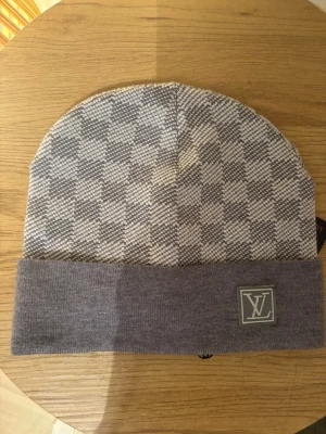 Gråmelerad Lw mössa - Snygg gråmelerad mössa från lw med klassiskt rutmönster och vikt kant. Lw-logga framtill på en patch. Tillverkad i mjukt stickat material som känns skönt mot huden. Perfekt accessoar för att lyfta din outfit.