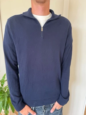 Mörkblå halvzip tröja - Mörkblå långärmad tröja med halv dragkedja och ståkrage. Tröjan har en enkel, stilren design och är tillverkad i ett mjukt, tunt material som passar perfekt till jeans eller chinos. Ribbstickade muddar vid ärmslut och nederkant ger en snygg passform.