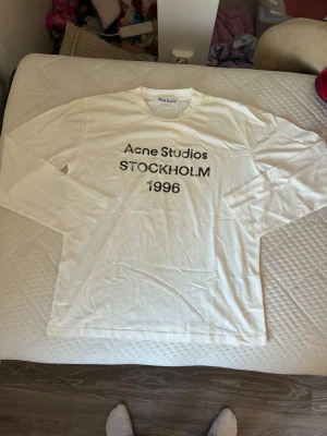 Vit långärmad topp Acne Studios - Vit långärmad topp från Acne Studios med tryck 'STOCKHOLM 1996' i svart framtill. Klassisk rund halsringning och relaxed fit. Perfekt för dig som gillar minimalistisk och stilren design. 10/10 skick riktigt feta nu till hösten 