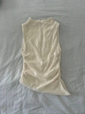  Ärmlös topp - Snygg vit topp med paljetter som ger ett glittrigt intryck. Toppen är ärmlös och har en hög hals samt dragkedja i ryggen. 