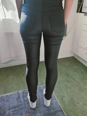 VERO MODA svarta byxor st M - Säljer ett par svarta coated leggings med hög midja och smal passform. De har bakfickor och detaljer som liknar jeans, men är stretchiga och sitter tight. Perfekta för dig som gillar en trendig och stilren look.