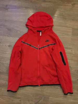 Röd Nike hoodie med dragkedja - Snygg röd hoodie från Nike med hel dragkedja framtill och svart Nike-logga på bröstet. Tappat lite färg på dragkedjan. 