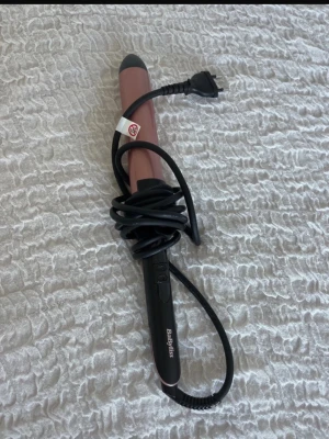 Rosa locktång från BaByliss - Säljer en rosa locktång från BaByliss med svart handtag och sladd. Perfekt för att fixa snygga lockar snabbt. Enkel att använda och har en smal, rundad form som gör det lätt att skapa olika frisyrer.