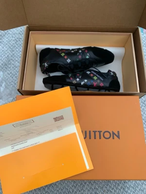 Louis Vuitton svarta sneakers - Svarta sneakers från Louis Vuitton med färgglada monogramdetaljer i rött, grönt, blått, vitt och gult. Skorna har en låg silhuett, snörning och detaljer i både läder och mocka. Perfekta för dig som vill sticka ut med exklusiv design.