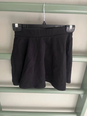 Svart skort från KappAhl - Säljer en svart skort från KappAhl i storlek 134/140. Skorten har en bred midjeresår och ett enkelt, stilrent utseende. Tillverkad i mjukt och stretchigt material som är bekvämt att bära. Perfekt för dig som vill ha både kjol-look och shortskomfort.