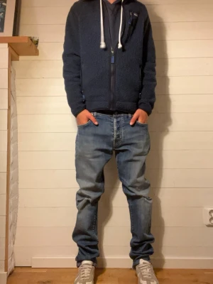 Blå raka jeans med slitningar - Säljer ett par blå jeans med raka ben och lätt slitna detaljer på knäna. Jeansen har klassisk femficksdesign och normal midja. Materialet är denim i bomull och passformen är avslappnad men ändå snyggt åtsittande. 