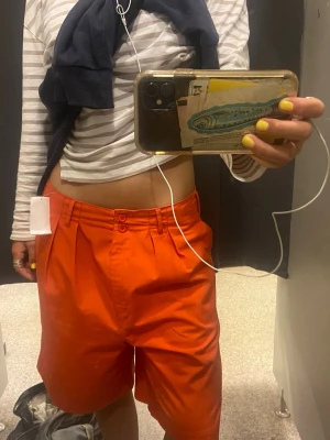 Lågmidjade shorts - Säljer ett par orangea shorts med låg midja och raka ben. Shortsen har två framfickor, en bakficka med knapp och stängs med dragkedja och knapp framtill. Perfekta för sommaren och riktigt snygga till en enkel t-shirt.