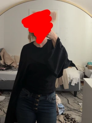 Svart långärmad topp med breda ärmar - En svart långärmad topp med rund halsringning och rak passform. Tillverkad i mjuk bomull, perfekt för en enkel och stilren look. Toppen har en klassisk design utan mönster eller extra detaljer.