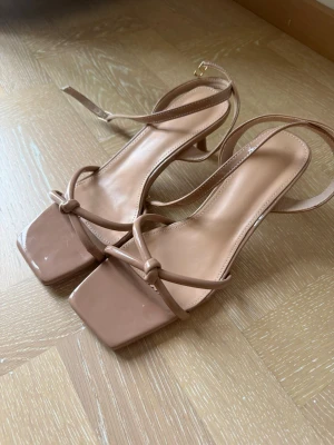 Beige sandaletter med fyrkantig tå - Säljer ett par super söta och stilrena sandaletter i beige med smala remmar och låg klack. Sandalerna har en blank finish och är aldrig använda endast testade.