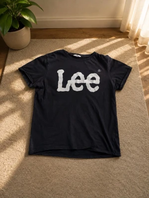 Svart Lee t-shirt med stor logga - Säljer en svart t-shirt från Lee med stor vit logga framtill. Klassisk rund halsringning och korta ärmar. Perfekt till jeans eller shorts för en avslappnad look. Det finns tecken på användning (se bilder)