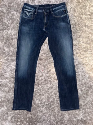 Replay anbass - Snygga mörkblå jeans med raka ben och diskreta slitningar framtill. Jeansen har klassiska fem fickor och kontrastsömmar. Materialet ser ut att vara denim med en något stretchig känsla. Perfekta för en avslappnad och trendig look.