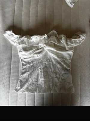 Vit offshoulder blus från SHEIN - Säljer en vit offshoulder blus från SHEIN i storlek XS. Blusen har ett vackert blommigt mönster i tyget och volangdetaljer vid axlarna. Materialet är lätt och har en elegant struktur som ger en romantisk vibe.