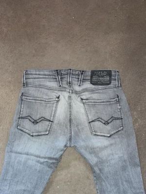 Ljusgrå slim fit jeans - Säljer ett par ljusgrå slim fit jeans med klassisk femficksmodell och snygga detaljer på bakfickorna. Jeansen har en något tvättad look och raka ben. Perfekta för dig som gillar en stilren och modern vibe. Jeansen är ifrån reaplay i modellen Anbass och har storleken 29/ 34