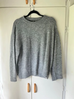 Grå stickad oversized tröja - Mysig grå stickad tröja med rund halsringning och avslappnad passform. Tröjan har långa ärmar och ribbstickade muddar vid ärmslut och nederkant. Perfekt för lager-på-lager och chill dagar.