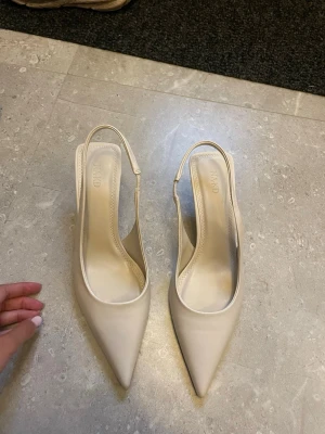 Beige pumps med öppen häl från NA-KD - Säljer ett par stilrena beige pumps från NA-KD med spetsig tå och öppen häl.  Aldrig använda!!