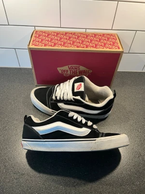 Vans Old Skool svartvita sneakers - Klassiska Vans Old Skool sneakers i svart och vitt med den ikoniska sidsvingen. Ovandel i mocka och canvas, vit gummisula med rutmönster undertill och vita snören. Perfekta för en streetwear-look och funkar till det mesta.