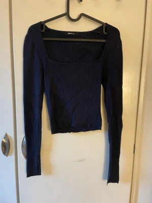 Mörkblå ribbad långärmad topp - Mörkblå ribbad topp med lång ärm och markant ringning. Modellen är croppad och har en slits i slutet av ärmen. Tillverkad i stretchigt material för en bekväm passform. Från Gina tricot i storlek S. 