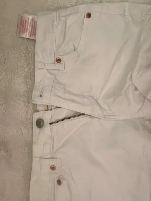 Vita Levi's jeans med raka ben - Snygga vita jeans från Levi's med klassisk femficksmodell och raka ben. Jeansen har silverfärgad knapp och dragkedja samt kopparfärgade nitar. Perfekta för en fräsch och stilren look.