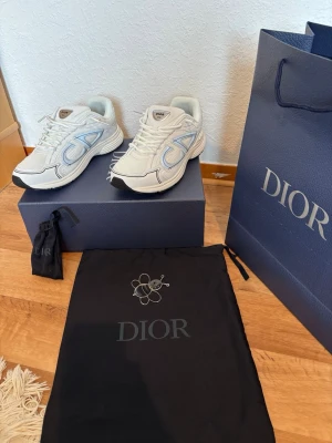 Dior b30 - Snygga vita Dior sneakers med reflekterande detaljer och meshpaneler. Skorna har en chunky sula, vita skosnören och tydliga Dior-loggor på sidan och plösen. Materialmix av mesh och läder ger en modern och sportig look.