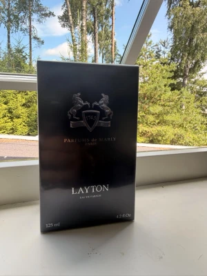 Parfums de Marly Layton EdP 125ml - Lyxig parfym från Parfums de Marly, Layton Eau de Parfum i en elegant mörkblå kartong med silverdetaljer och två hästar på framsidan. Flaskan innehåller 125 ml och doften är känd för sin exklusiva och sofistikerade karaktär.