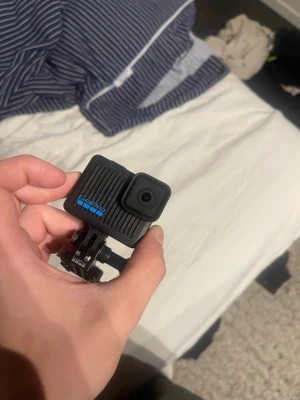 GoPro HERO10  - GoPro HERO10 är en kompakt och tålig actionkamera i svart plast med en fyrkantig form och lins i hörnet. Kameran har tydliga blå HERO10-loggor och ett robust fäste för montering på hjälm eller cykel. Perfekt för äventyr och sport.