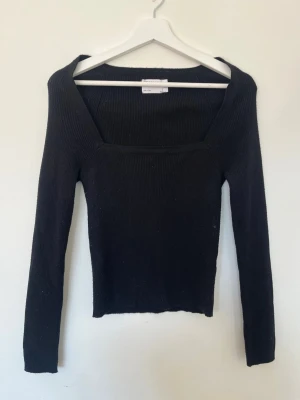 Svart ribbad långärmad topp - En svart, ribbad långärmad topp med fyrkantig ringning. Toppen är figurnära och har en stilren, minimalistisk look som passar till många olika outfits. Perfekt för dig som gillar enkla men snygga basplagg.