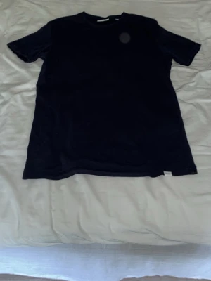 Mörkblå t-shirt från Les Deux - En stilren mörkblå t-shirt från Les Deux med rund halsringning och diskret broderad logga på bröstet. Tillverkad i mjuk bomull och har en klassisk passform med korta ärmar. Perfekt till jeans eller shorts för en clean look.