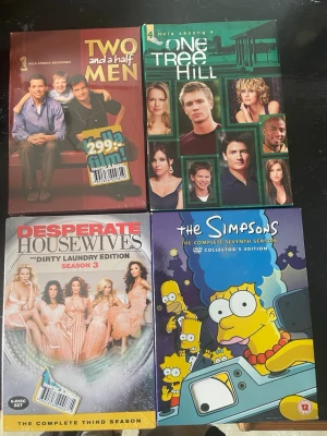 Fyra boxar med TV-serier på DVD - Säljer fyra DVD-boxar med populära TV-serier: Two and a Half Men, One Tree Hill, Desperate Housewives och The Simpsons. Omslagen är färgglada med bilder på karaktärerna och logotyper. Perfekt för dig som gillar klassiska serier och vill ha dem i samlingen.2 av dem är ej upptagna inplastade 