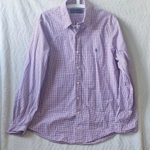 Rutig skjorta från Ralph Lauren L - Klassisk långärmad skjorta från Ralph Lauren i röd, blå och vit rutig bomull. Skjortan har button-down krage, knäppning framtill och en liten broderad logga på bröstet. Perfekt för en stilren och avslappnad look.