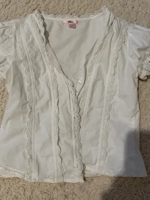 Vit blus med spets från Gina Tricot 14+ avdelning  - Söt vit blus från Gina Tricot med korta armar. Blusen har v-ringning och knappar framtill, vilket ger en romantisk och vintageinspirerad look. Perfekt att styla med jeans. Storlek kan vara lite oklar men jag skulle säga att en som bär S kan ha den då den var alldeles för tajt vid armhålorna för mig som bär storlek M, använt några enstaka gånger. Max 3.
