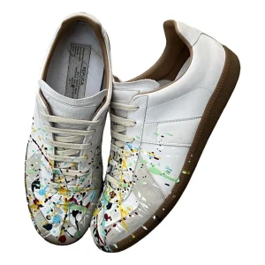 Masion Margiela Paint Splatter  - Unika vita sneakers med coola färgstänk i blått, gult, rött och grönt. Skorna har beige snörning och en brun sula. Perfekt för dig som vill sticka ut med din stil och gillar konstnärliga detaljer.