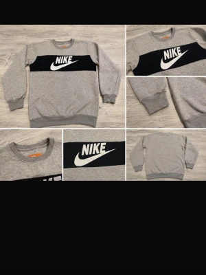 Grå sweatshirt från Nike - Grå sweatshirt från Nike med svart panel och stor vit logga framtill. Tröjan har rund halsringning, långa ärmar och ribbade muddar vid ärmslut och nederkant. Perfekt för en sportig och avslappnad stil.  