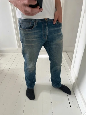Blå Replay jeans (W32 L34) - Säljer ett par blå jeans från Replay med snyggt tvättad och sliten look. Klassisk femficksmodell med raka ben och normal midja. Jeansen är gjorda i denim och har detaljer som nitar och kontrastsömmar. Perfekta för dig som gillar en avslappnad stil.