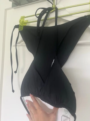Svart bikiniöverdel med knyt - Snygg svart bikiniöverdel med knyt i nacken och ryggen. Enkel och stilren design som passar perfekt till stranden eller poolen. Bikinin har trekantsformade kupor och tunna band för justerbar passform.