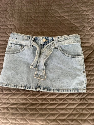 Ljusblå jeanskjol med bälte - Trendig ljusblå jeanskjol i kort modell med tillhörande bälte i samma denimtyg. Kjolen har klassiska fickor fram och bak samt hällor för bältet. Perfekt för dig som gillar en avslappnad men snygg stil.