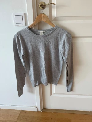 Ljusgrå basic tröja med rund hals - En enkel och stilren ljusgrå tröja med rund halsringning och långa ärmar. Tröjan är tillverkad i ett mjukt och tunt material, perfekt för lager på lager eller som den är. Passar till det mesta och har en klassisk, clean look.